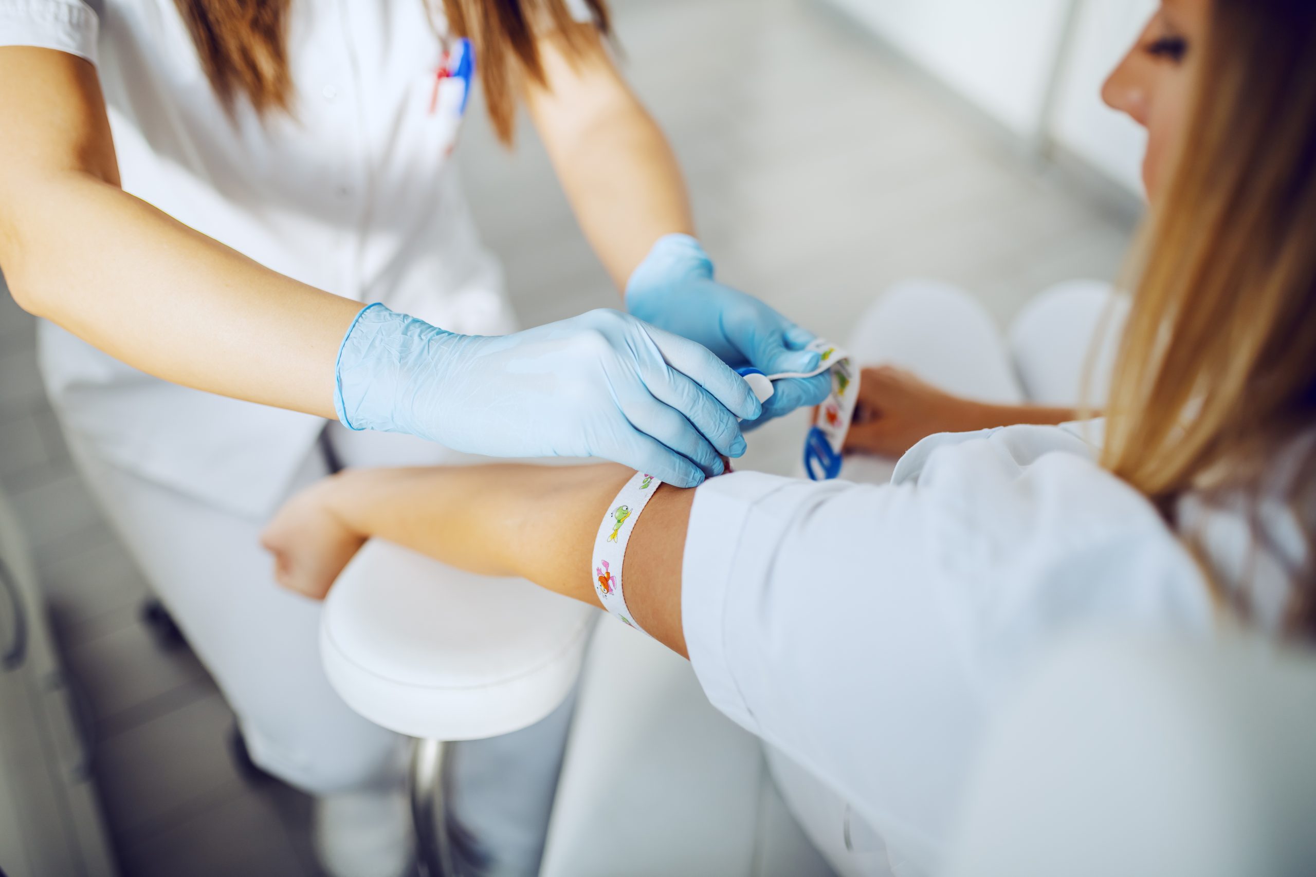 Cropped picture of lab assistant putting band on patient's arm and preparing for blood sampling.